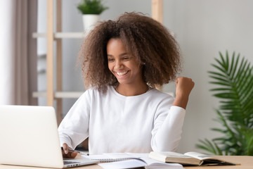 Excited overjoyed african teen girl student winner looking at laptop