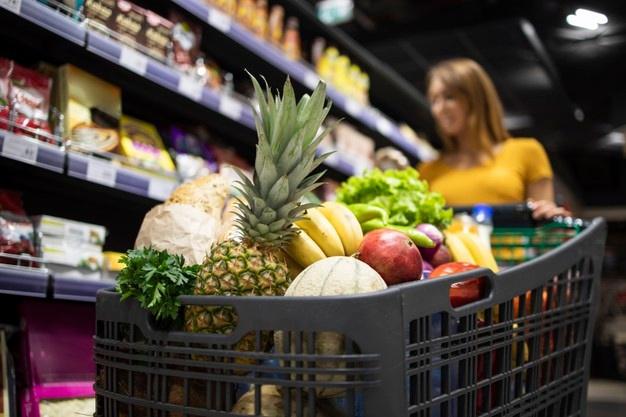 Close up view of shopping cart overloaded with food while in background female person choosing products Free Photo