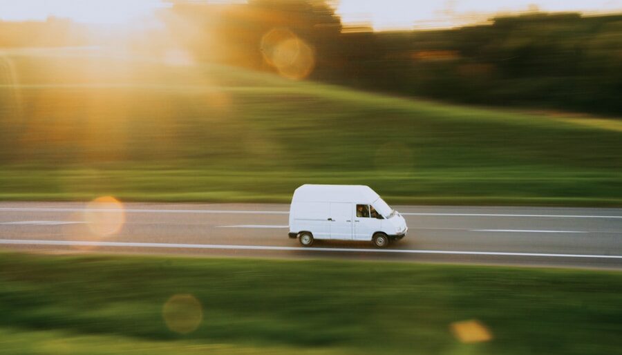 a white van driving down a road next to a lush green field