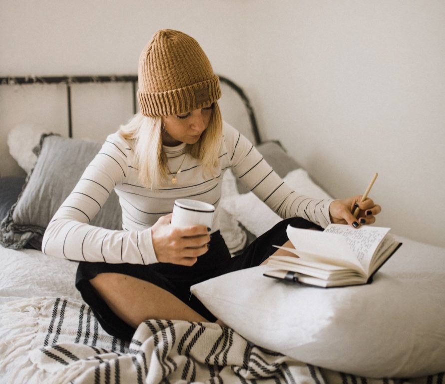 woman in striped shirt sitting on bed while writing